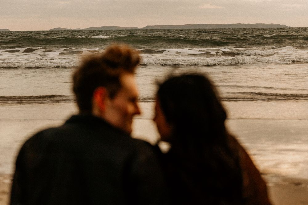 A silhouetted couple gazes at the ocean waves during sunset at the beach.