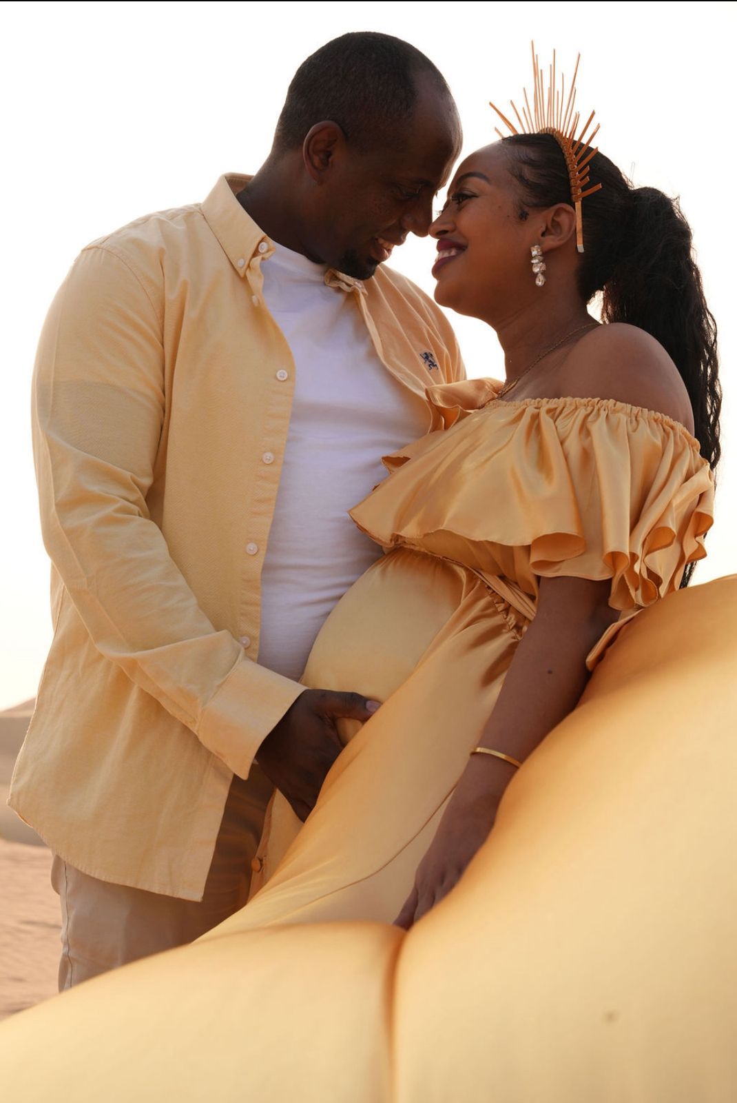 Romantic outdoor maternity photo showing a couple in matching peach outfits sharing an intimate moment at sunset.