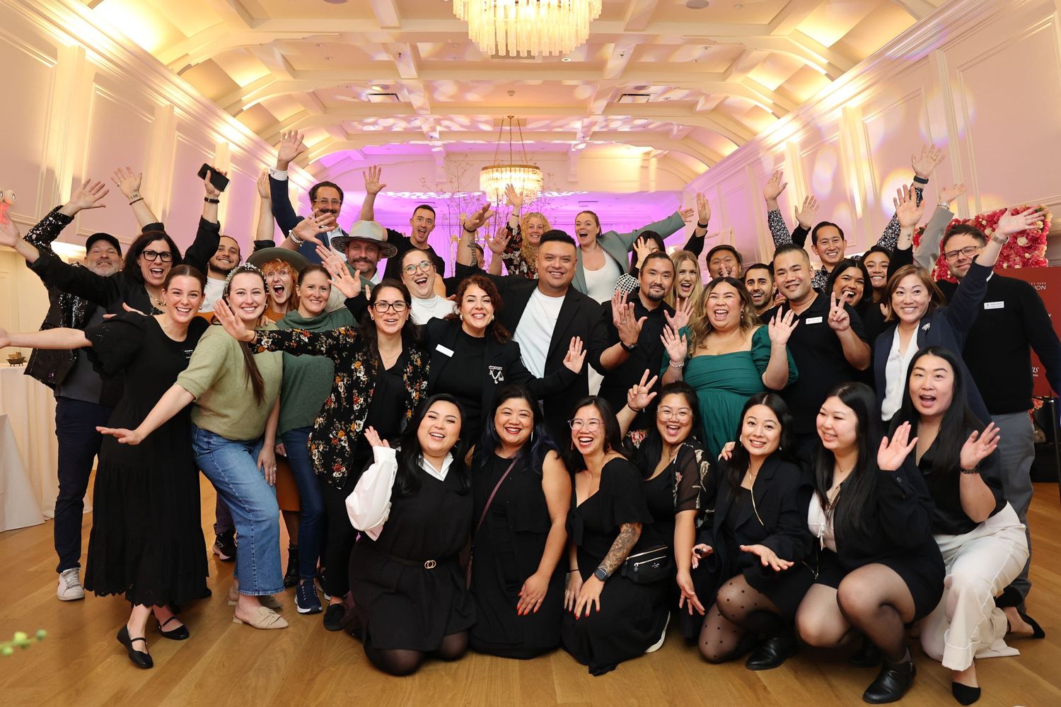 Large group celebrating at an elegant ballroom event with purple mood lighting.