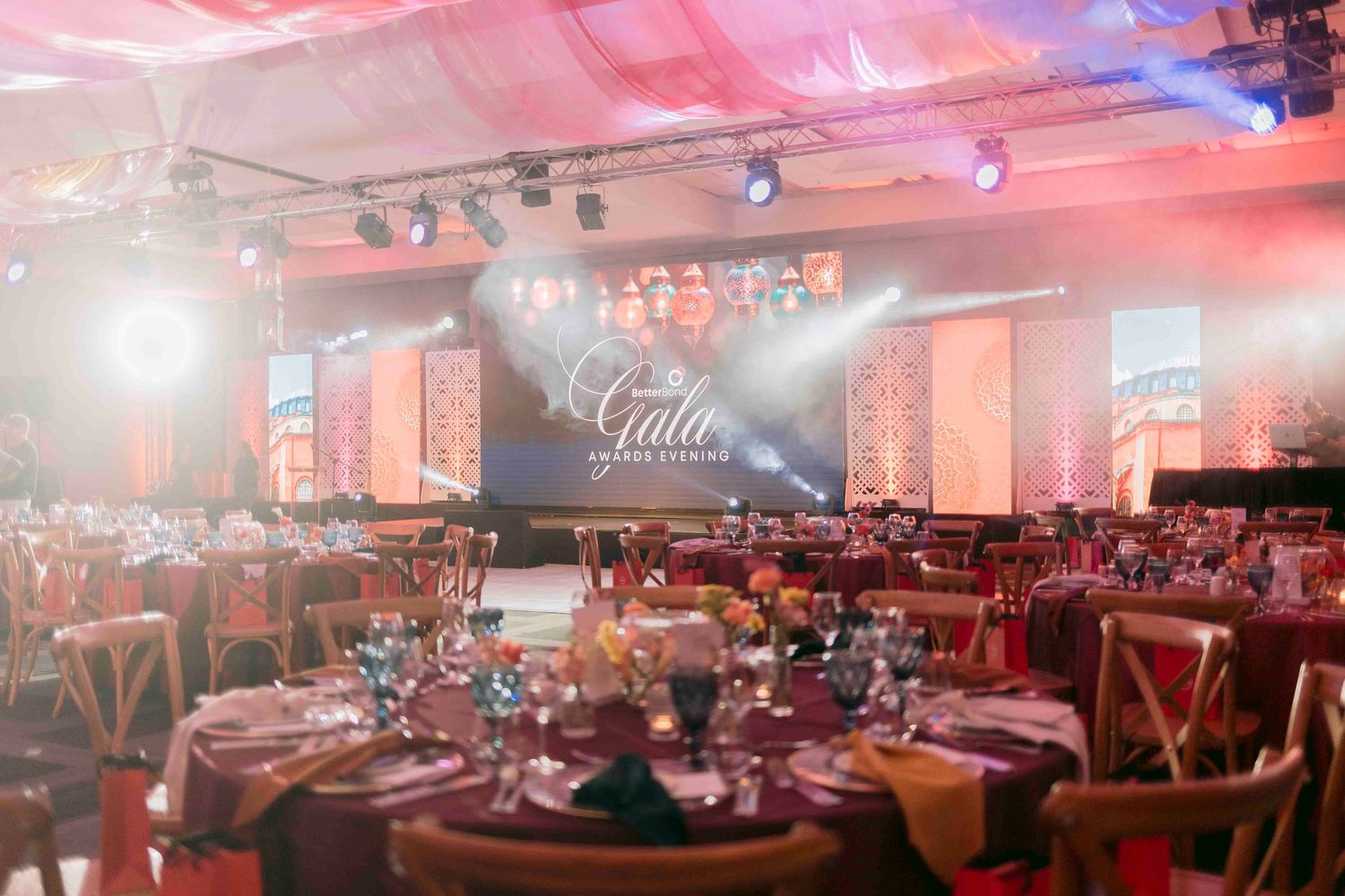 Elegant gala dinner venue with round tables, formal settings, and dramatic stage lighting.