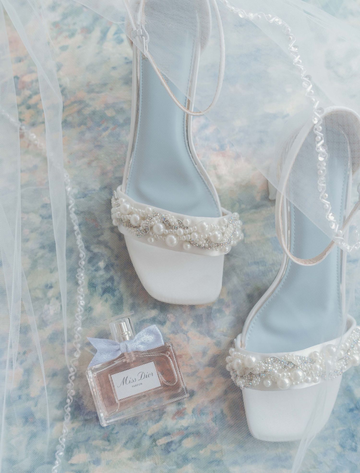 Elegant white pearl-embellished wedding sandals displayed with a delicate perfume bottle on a soft blue background.
