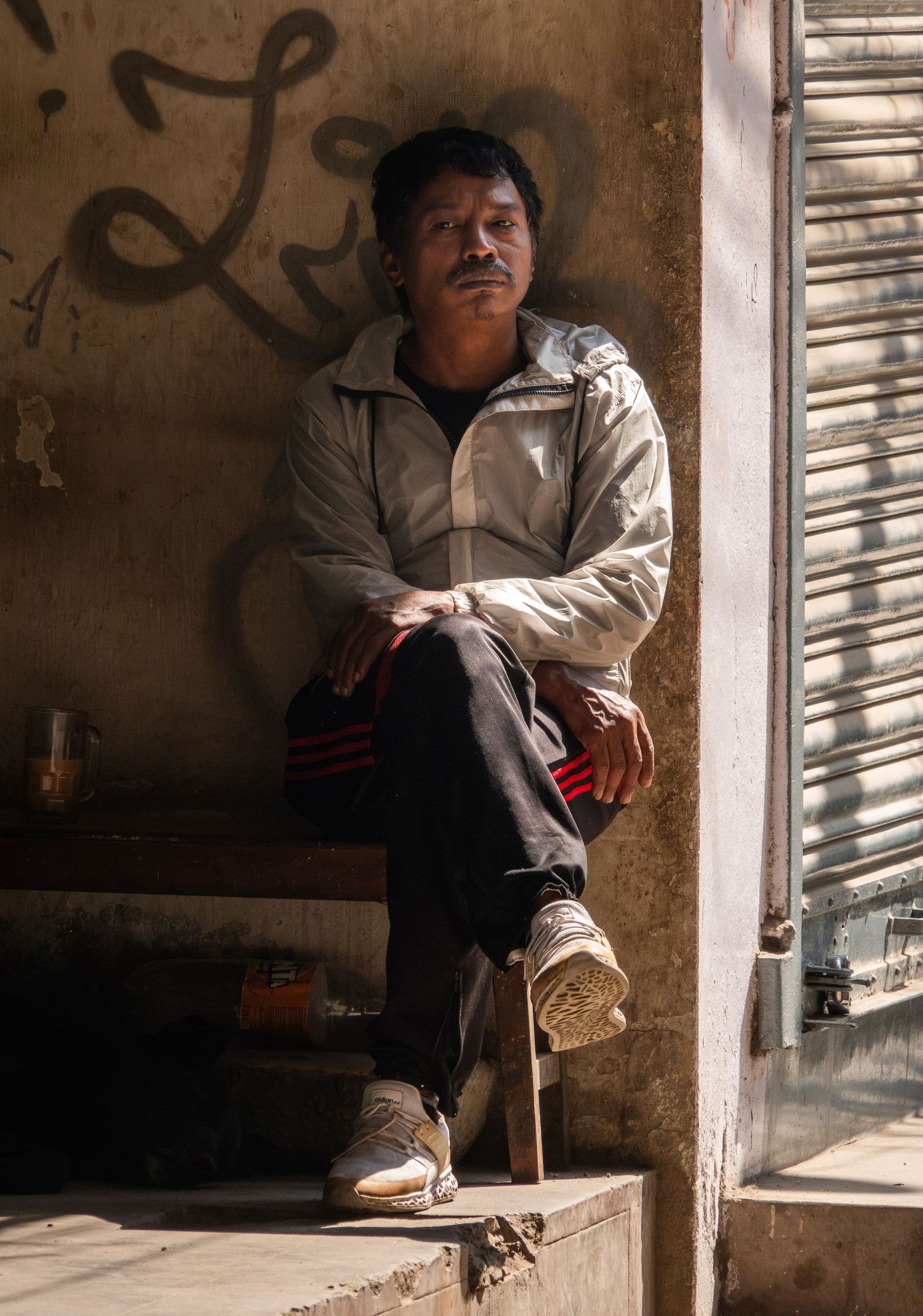 A person sits casually on a concrete step against a weathered wall with graffiti.