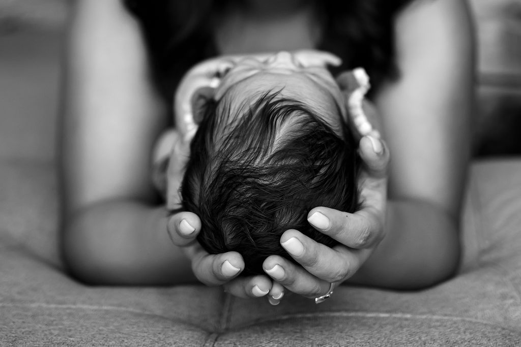 BLACK AND WHITE IMAGE, THE TOP OF A NEWBORNS HEAD, CRADLED IN A WOMANS ARMS.  mACRO SHOT