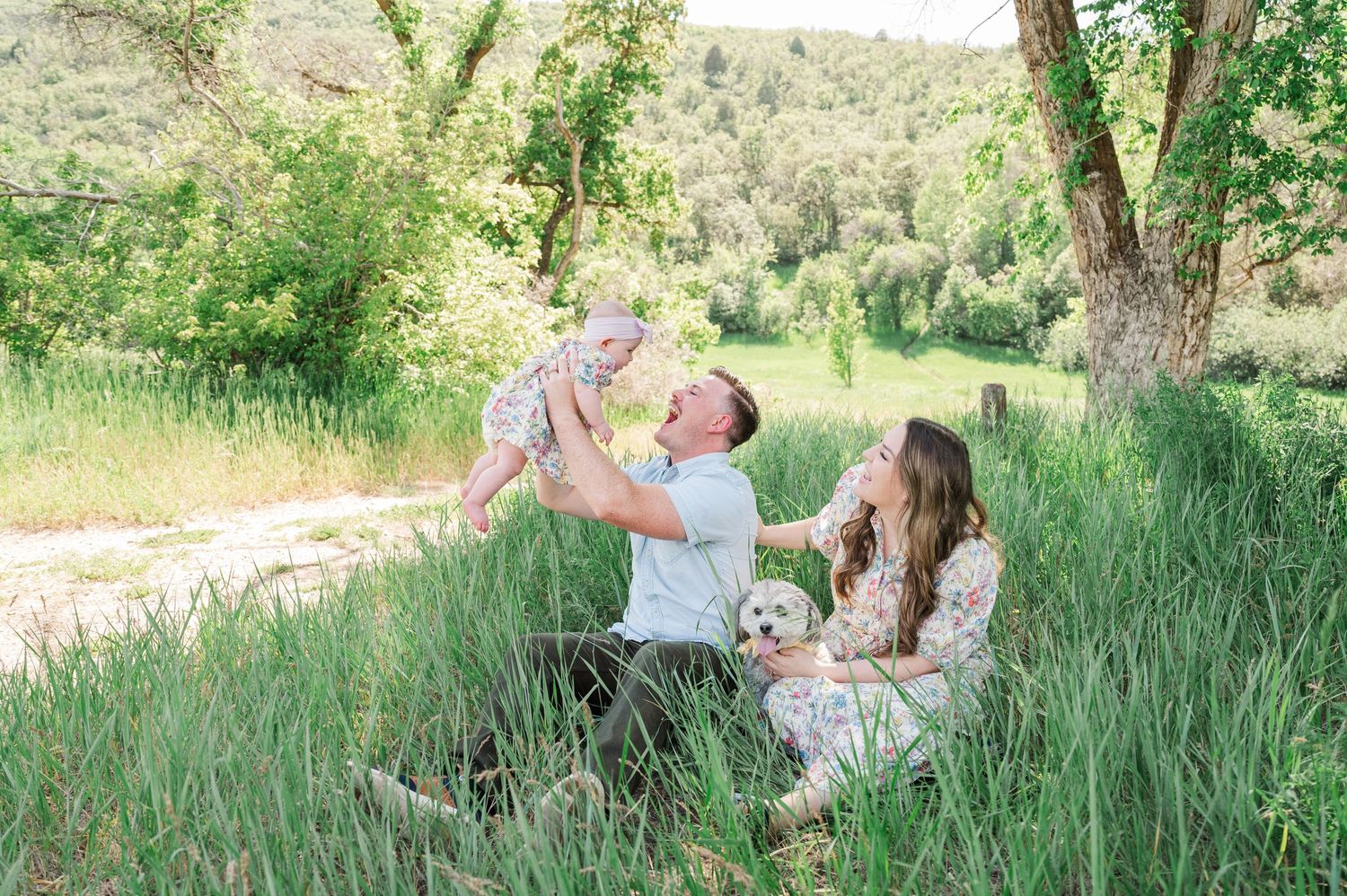 Family enjoying playful moments together in a serene outdoor setting with tall grass.