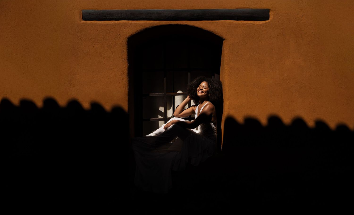 A silhouetted figure in a window frame against warm lighting and shadows.