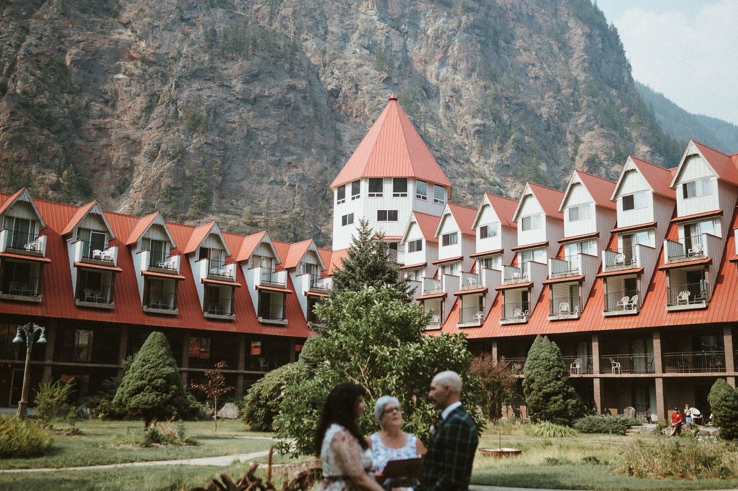A majestic hotel with red-roofed architecture nestled against towering mountain cliffs.