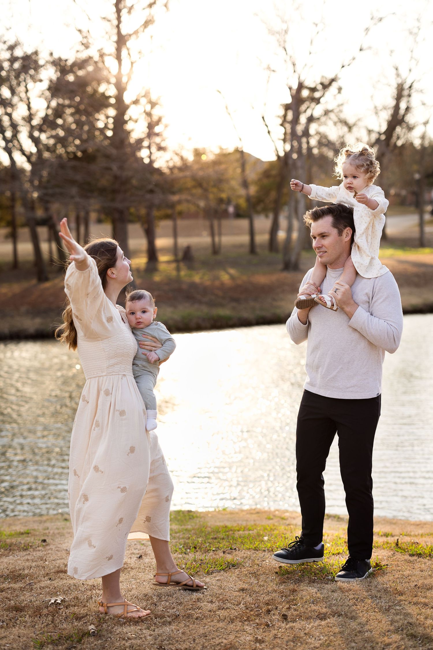A family playfully dances together at sunset by a lake, with golden light filtering through trees in the background.