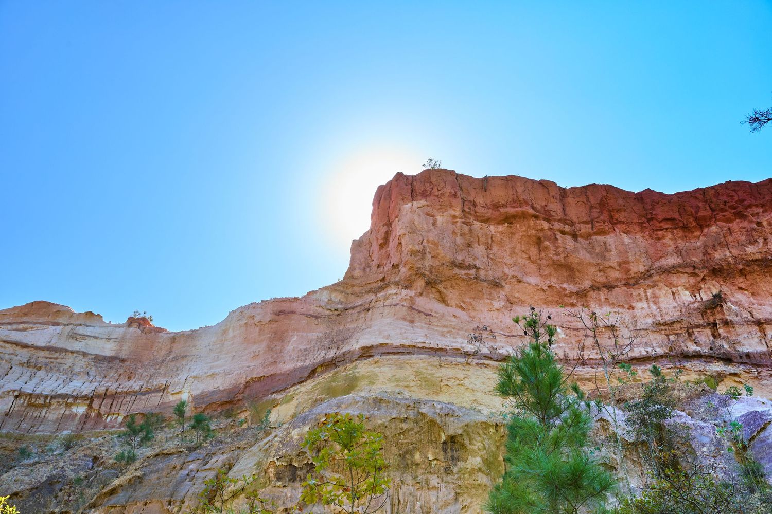 Sunlit red rock canyon wall against bright blue sky.