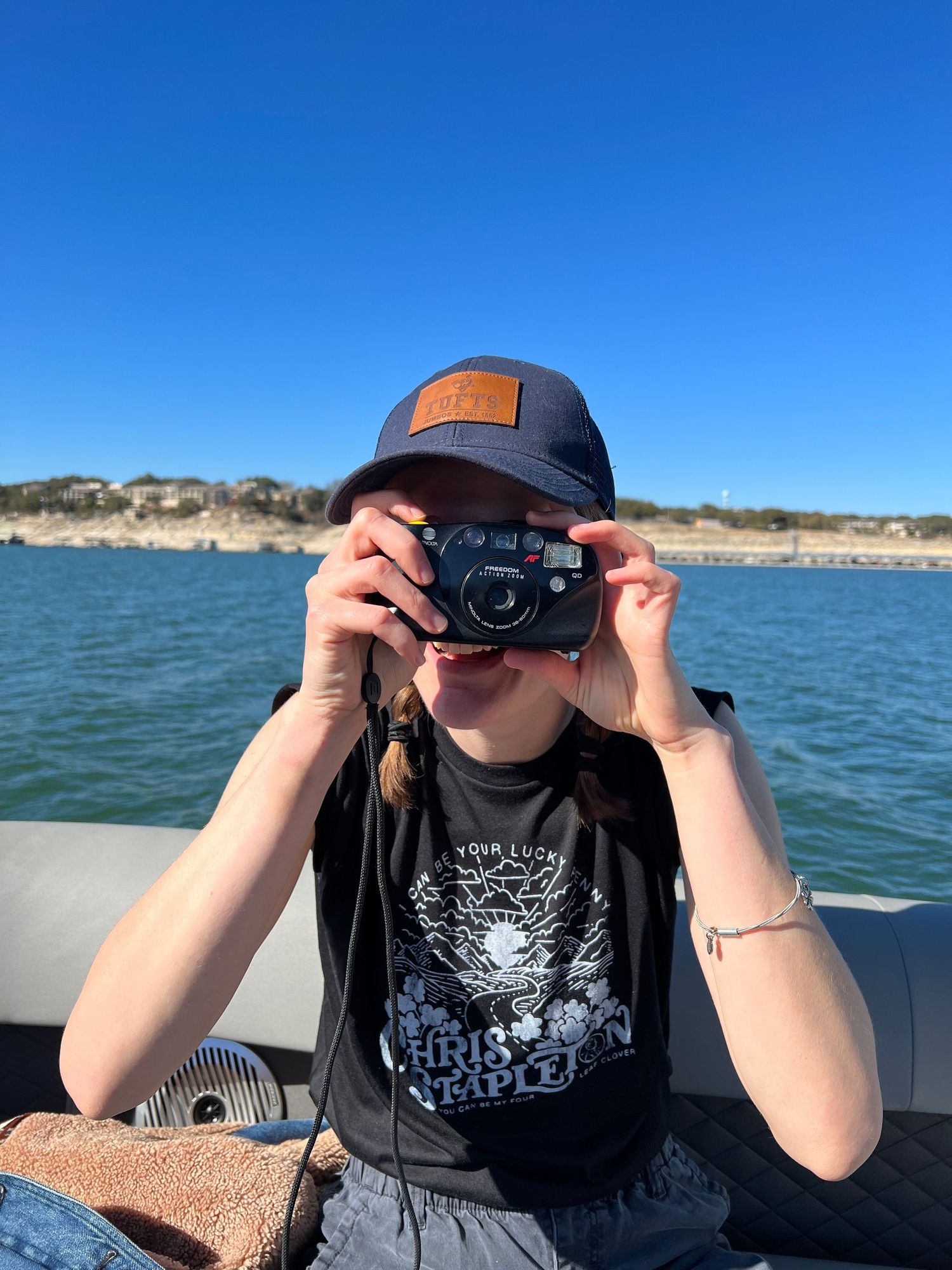 Person taking photo with vintage camera on boat with lake and cliffs in background.