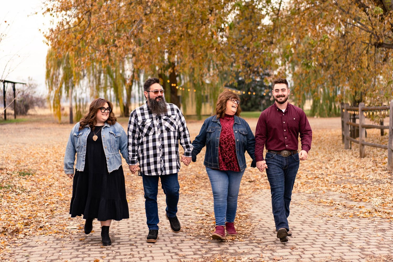 A group enjoying an autumn walk together on a leaf-covered path under golden willow trees in a park.