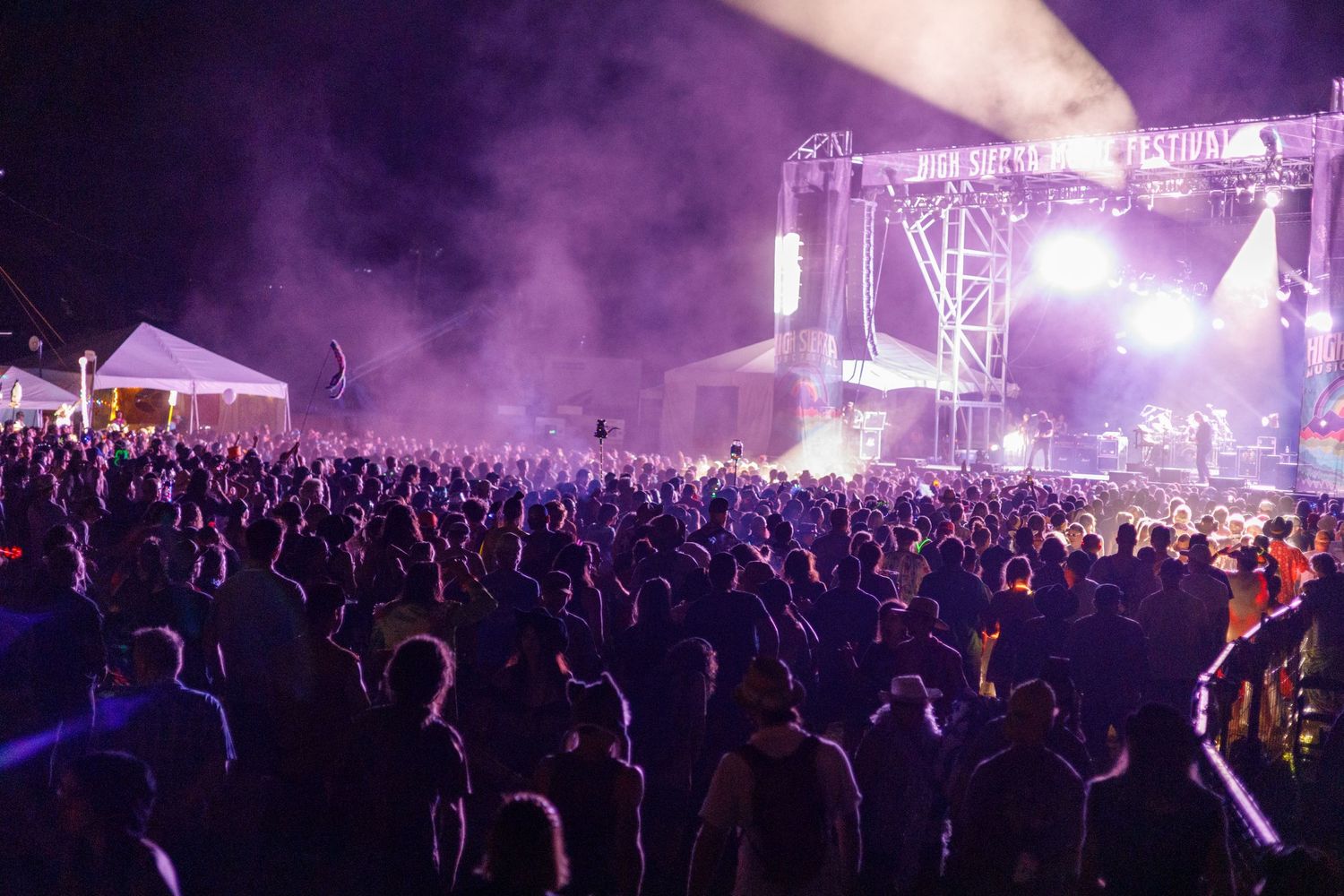 Silhouetted crowd watches concert stage with purple lighting and fog effects.