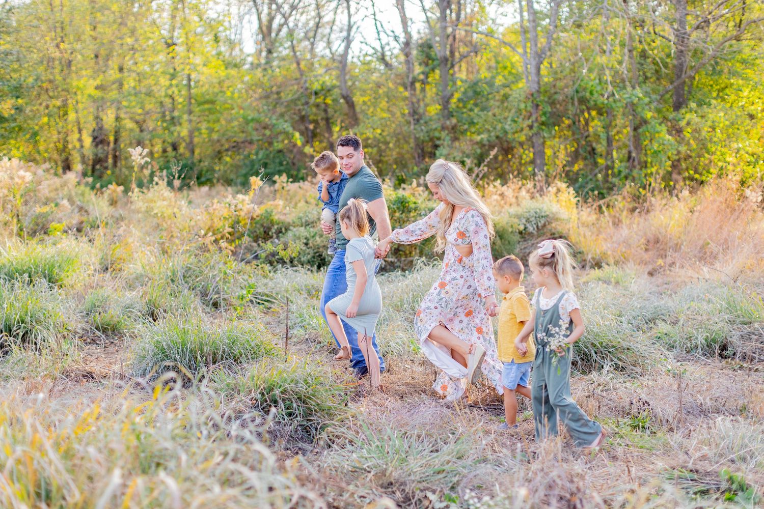 A cheerful group enjoys dancing and playing together in a sunlit autumn field surrounded by golden grass and trees.