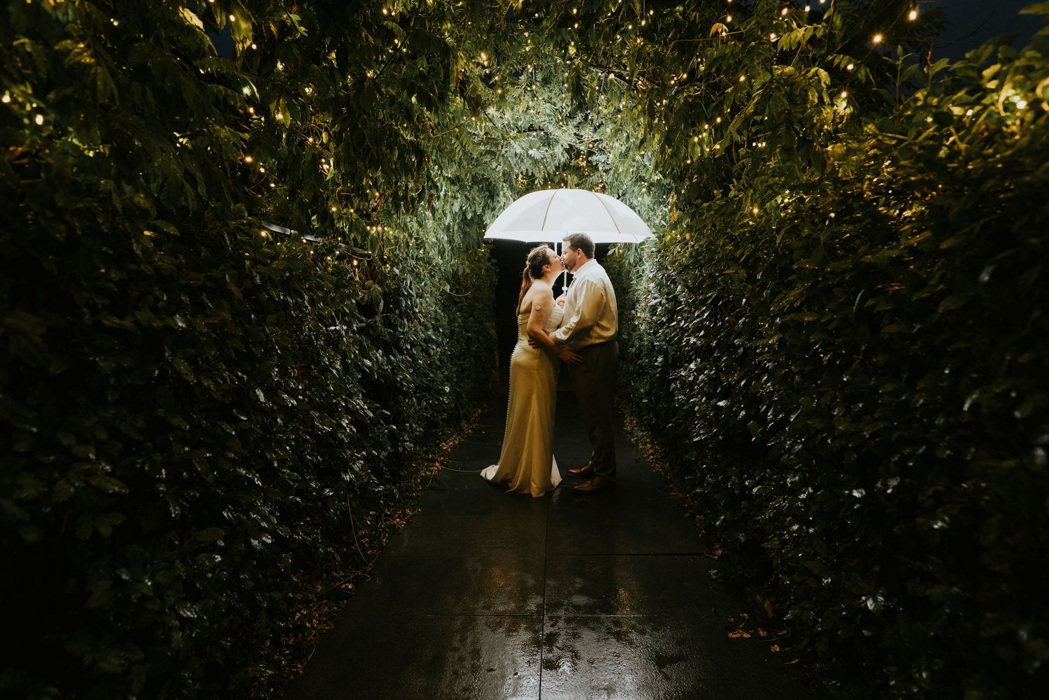 Wedding couple poses among lush greenery and white floral arrangements outdoors.