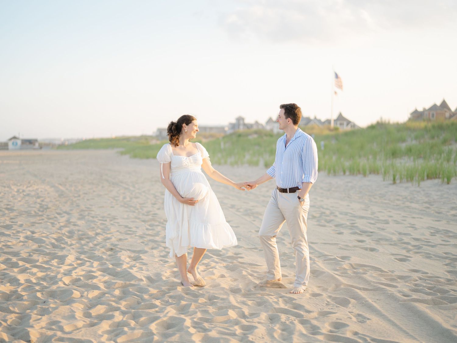 Expecting couple walking hand in hand along Ocean Grove NJ shoreline during golden hour maternity session.