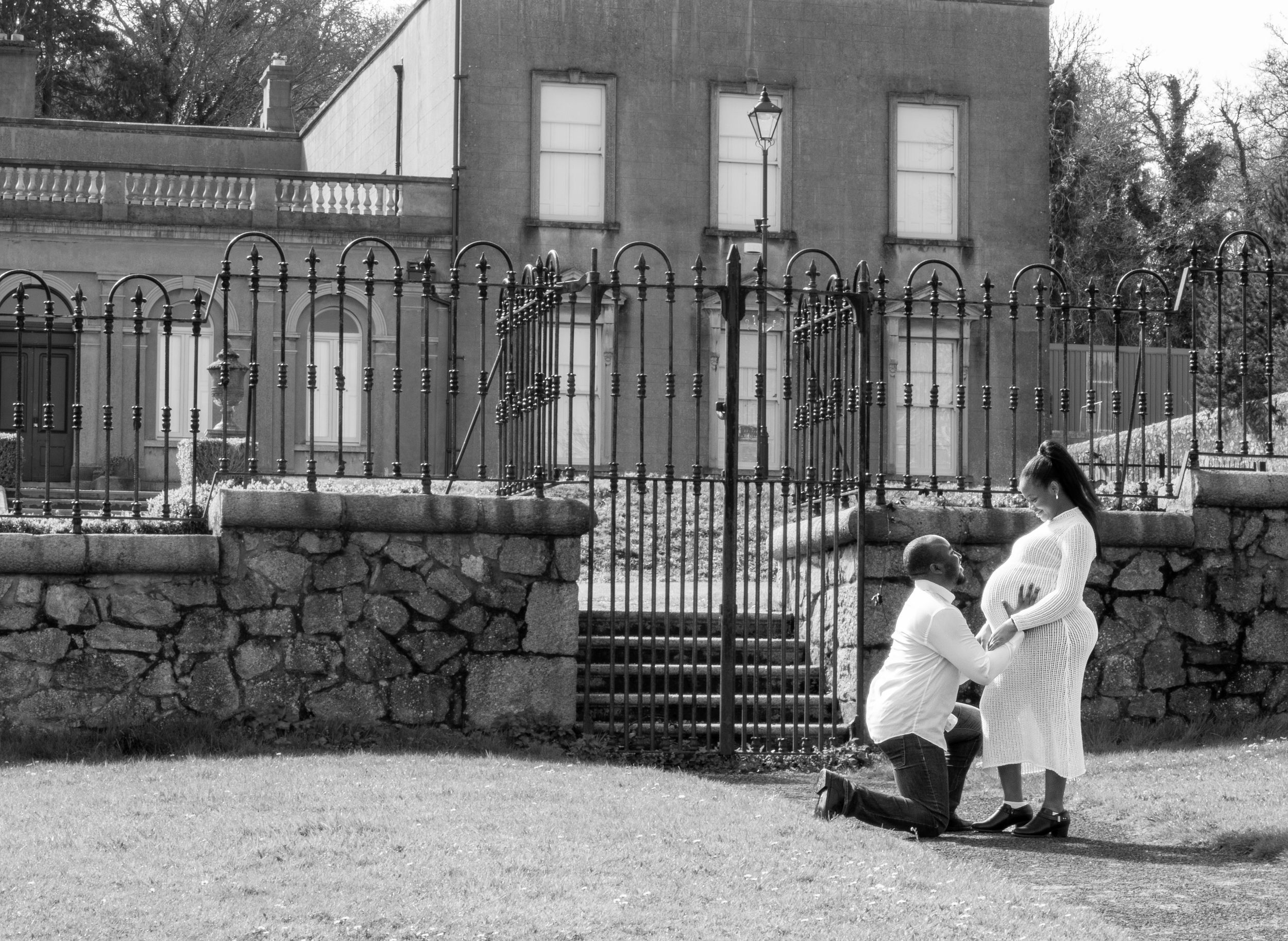 Vintage black and white photo of people by iron gate and stone wall.
