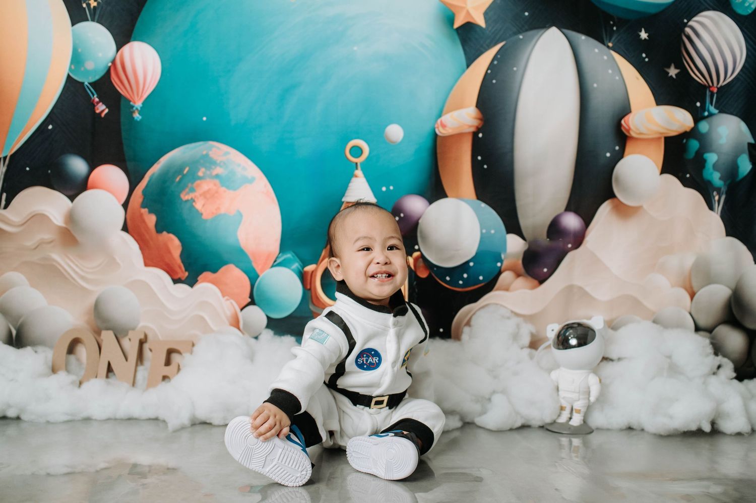 Space-themed birthday setup with white clouds, astronaut decor, and colorful balloon backdrop.