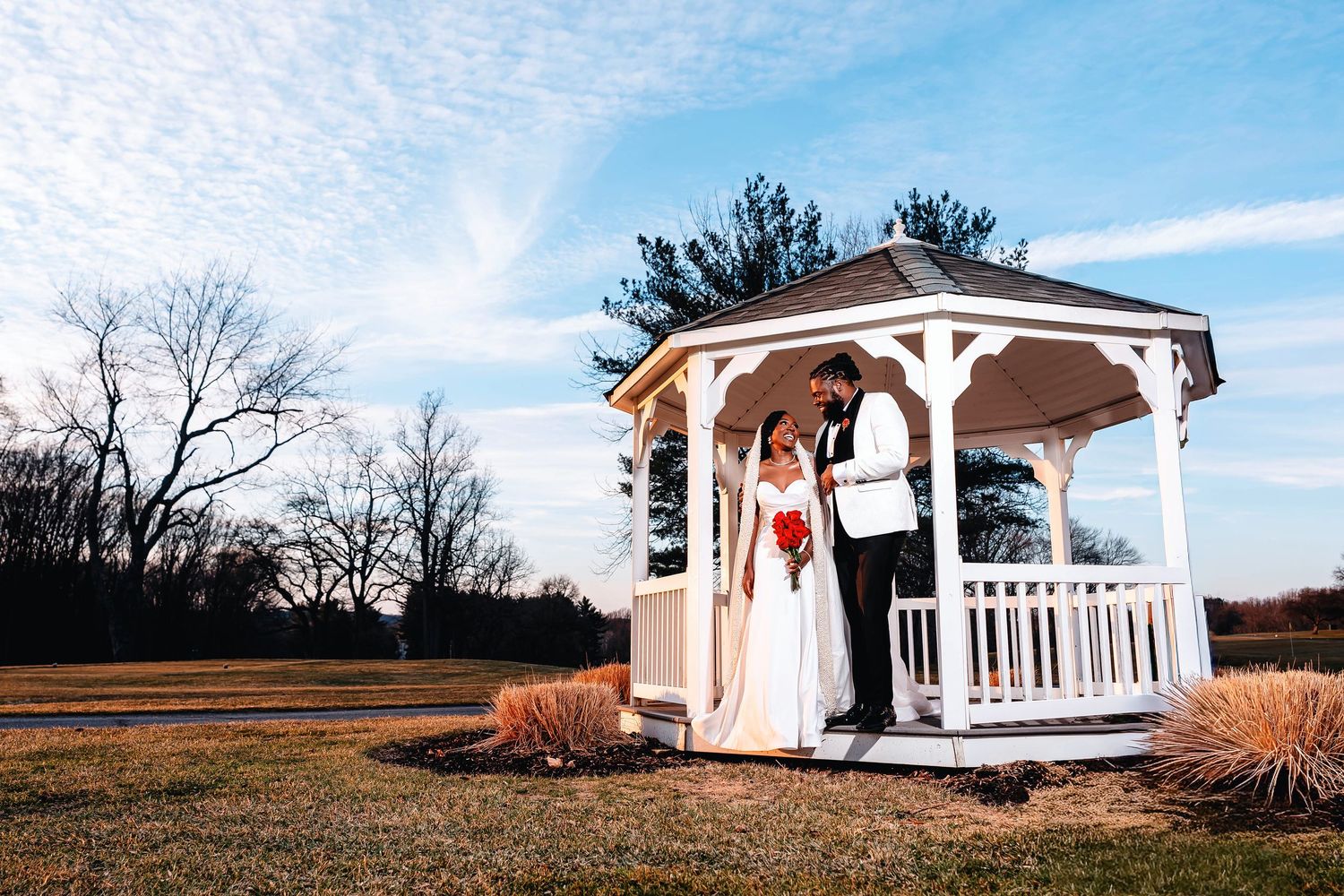 Bride and groom pose romantically in a white gazebo on a sunny winter wedding day with blue skies. Deerfield Golf Club Newark De