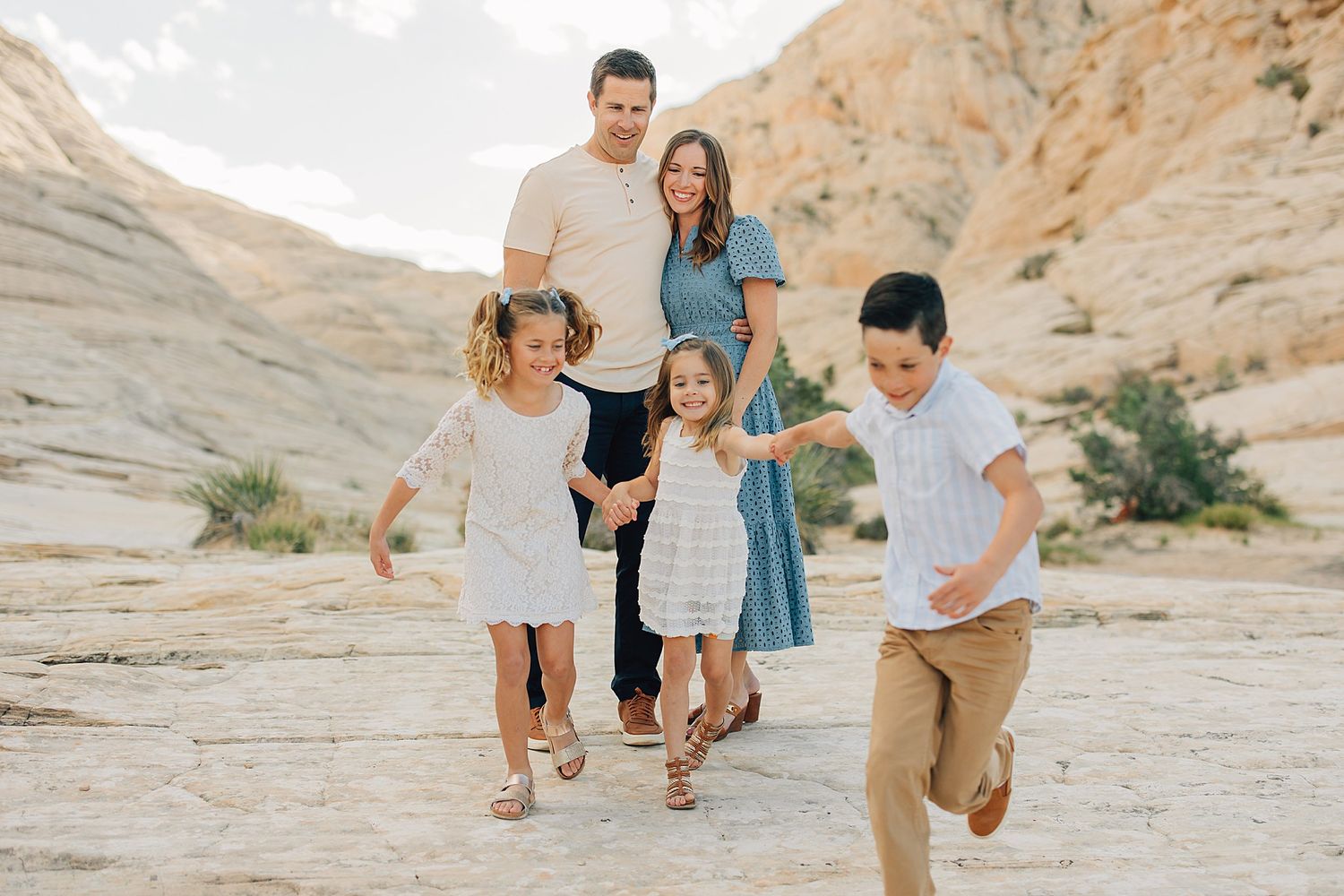 Happy family of five posing together in a scenic desert landscape with sandy cliffs and a pond.