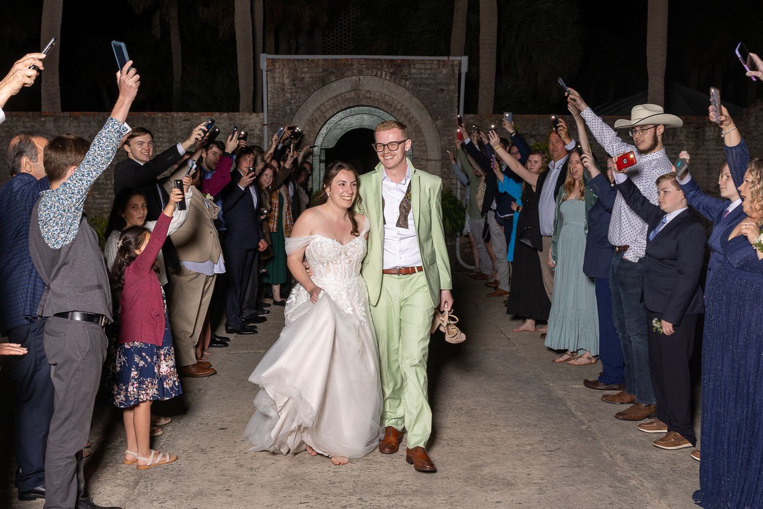 Bride and groom exit wedding ceremony through cheering guests holding sparklers at night.