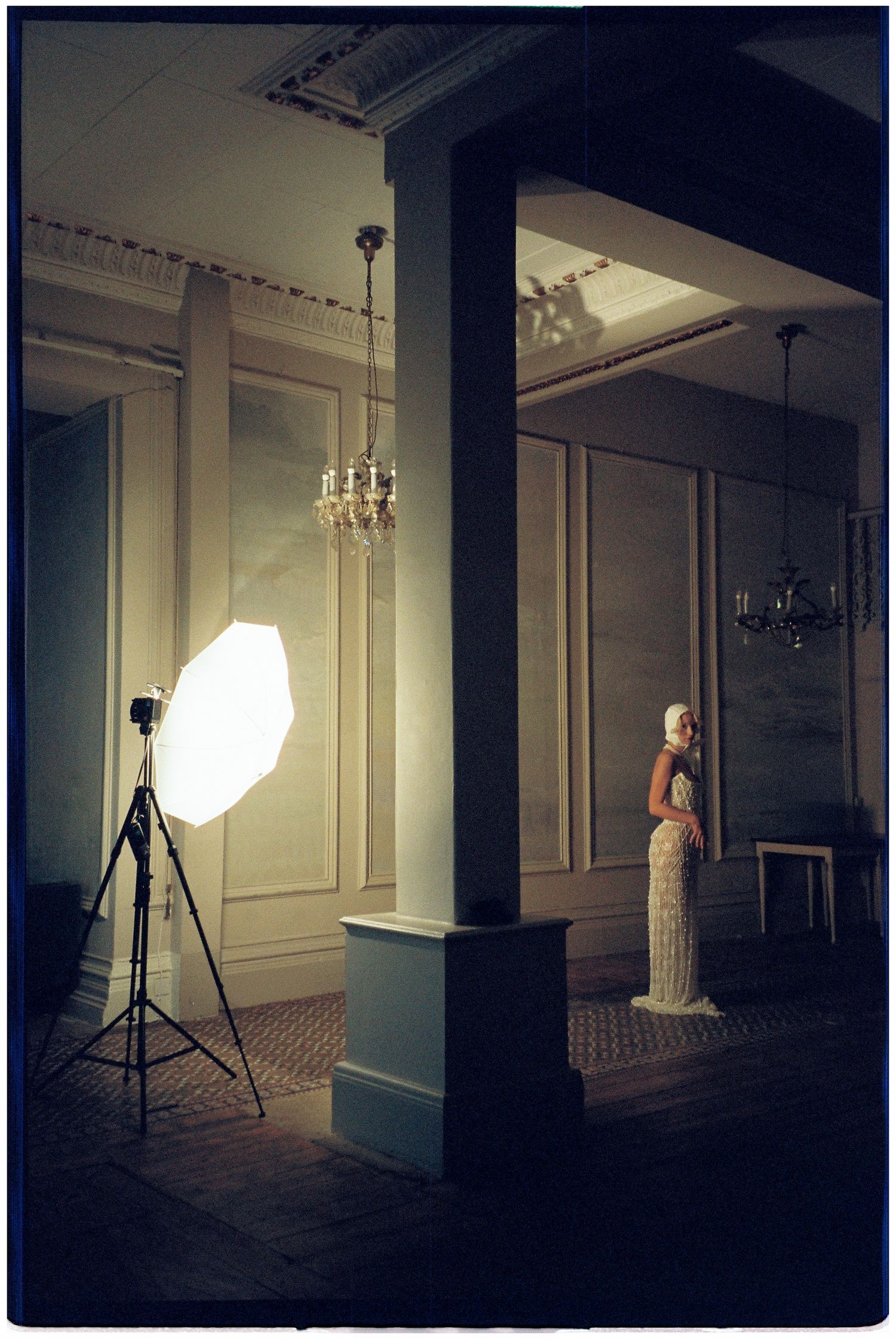 Two figures in elegant evening attire dance together in an ornate ballroom with chandeliers and decorative moldings.