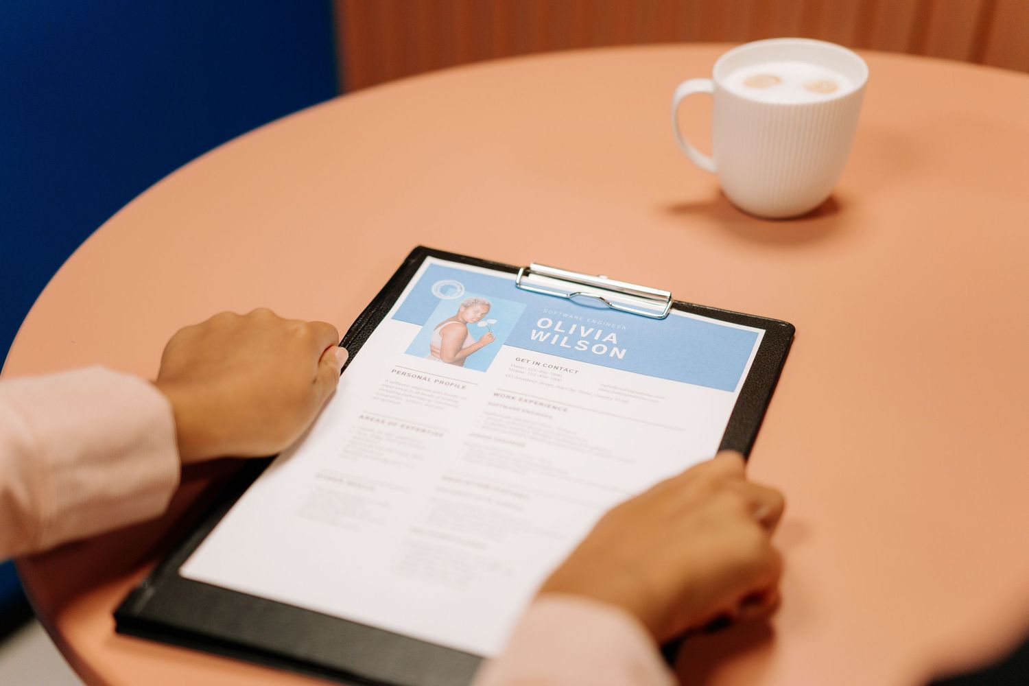 Person reviewing a professional resume on a clipboard at a round table with a white coffee cup nearby.