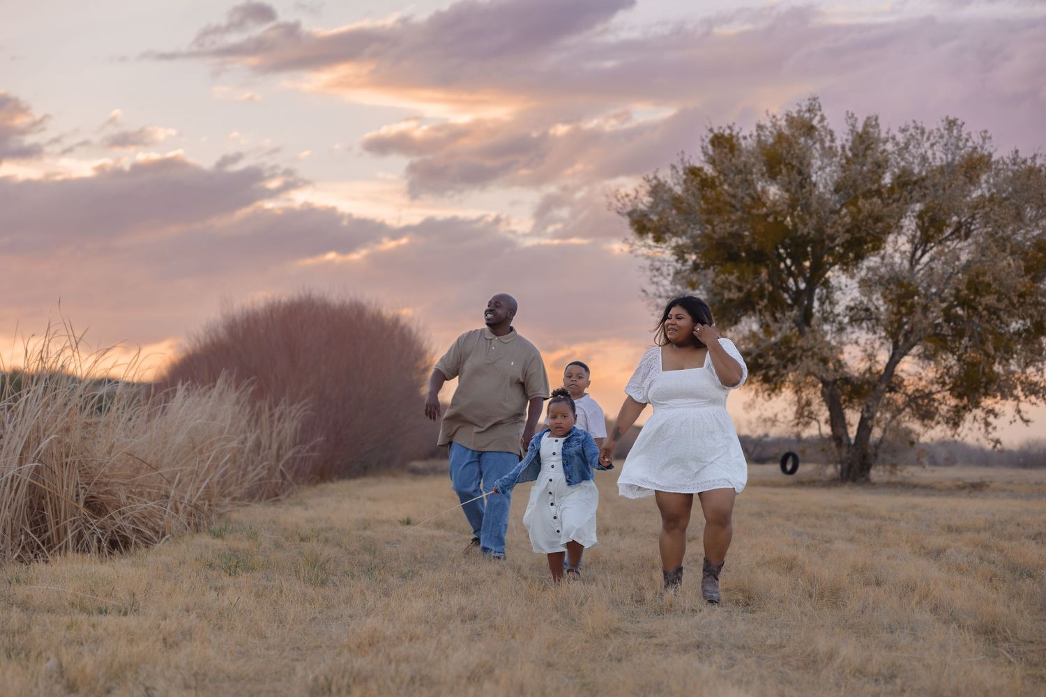 Family members walk together through a golden field at sunset, silhouetted against a colorful sky.