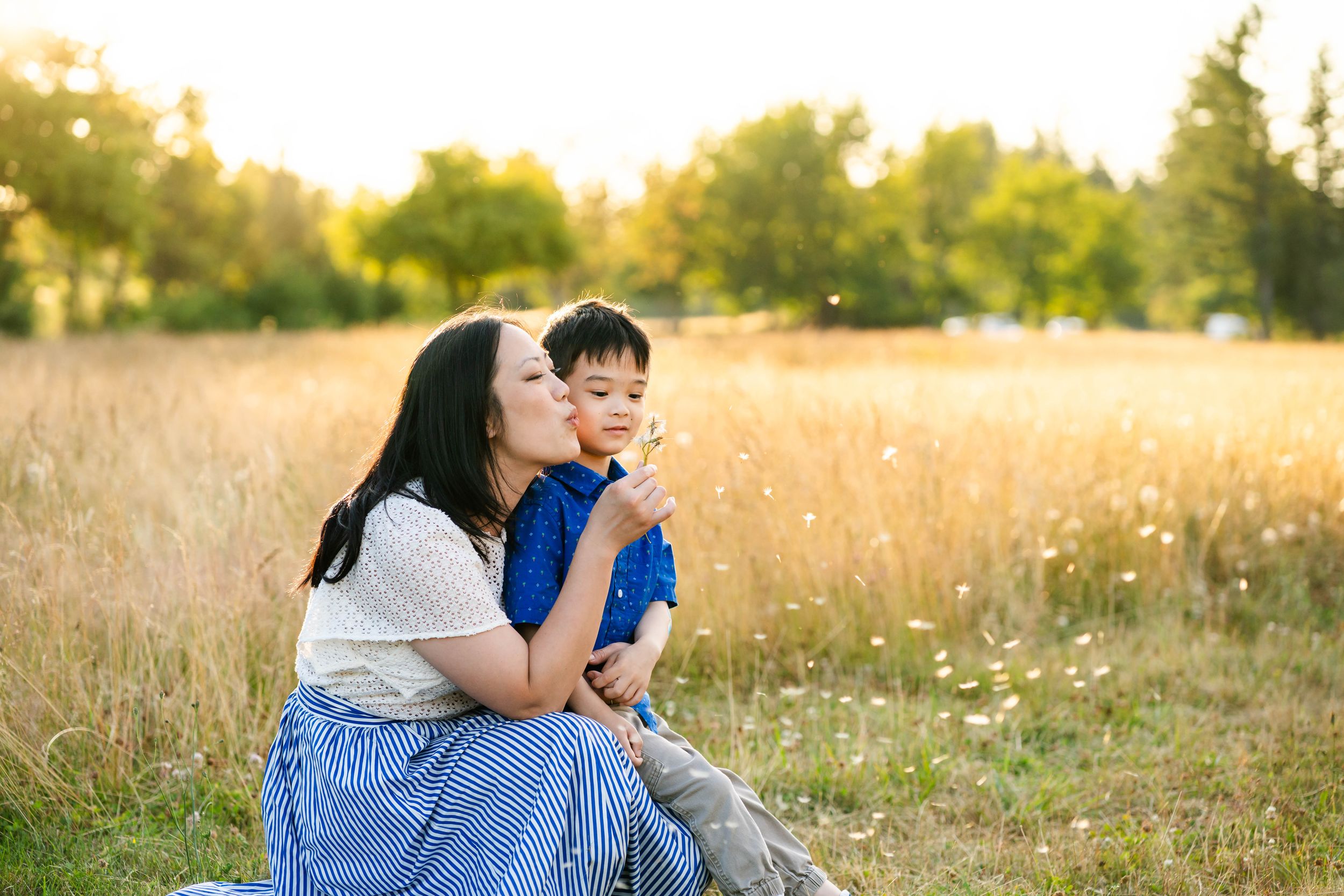 Mother and son blow dandelion puffs.