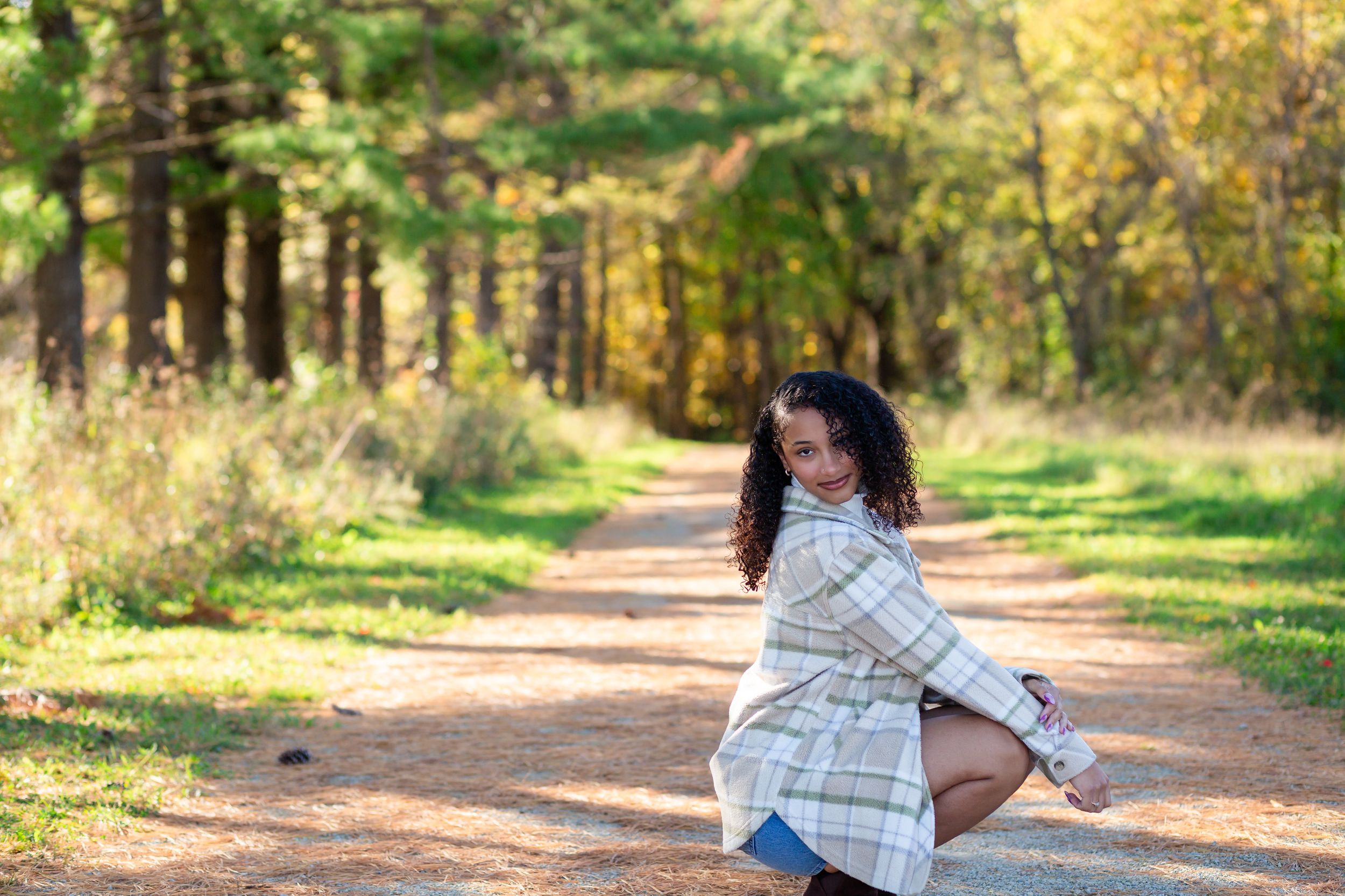 A person in a white sweater walks along a scenic autumn forest trail surrounded by golden foliage and sunlight.