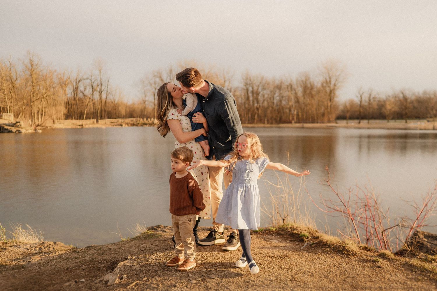 A family shares a tender moment together on a lakeside hill during golden hour sunset.