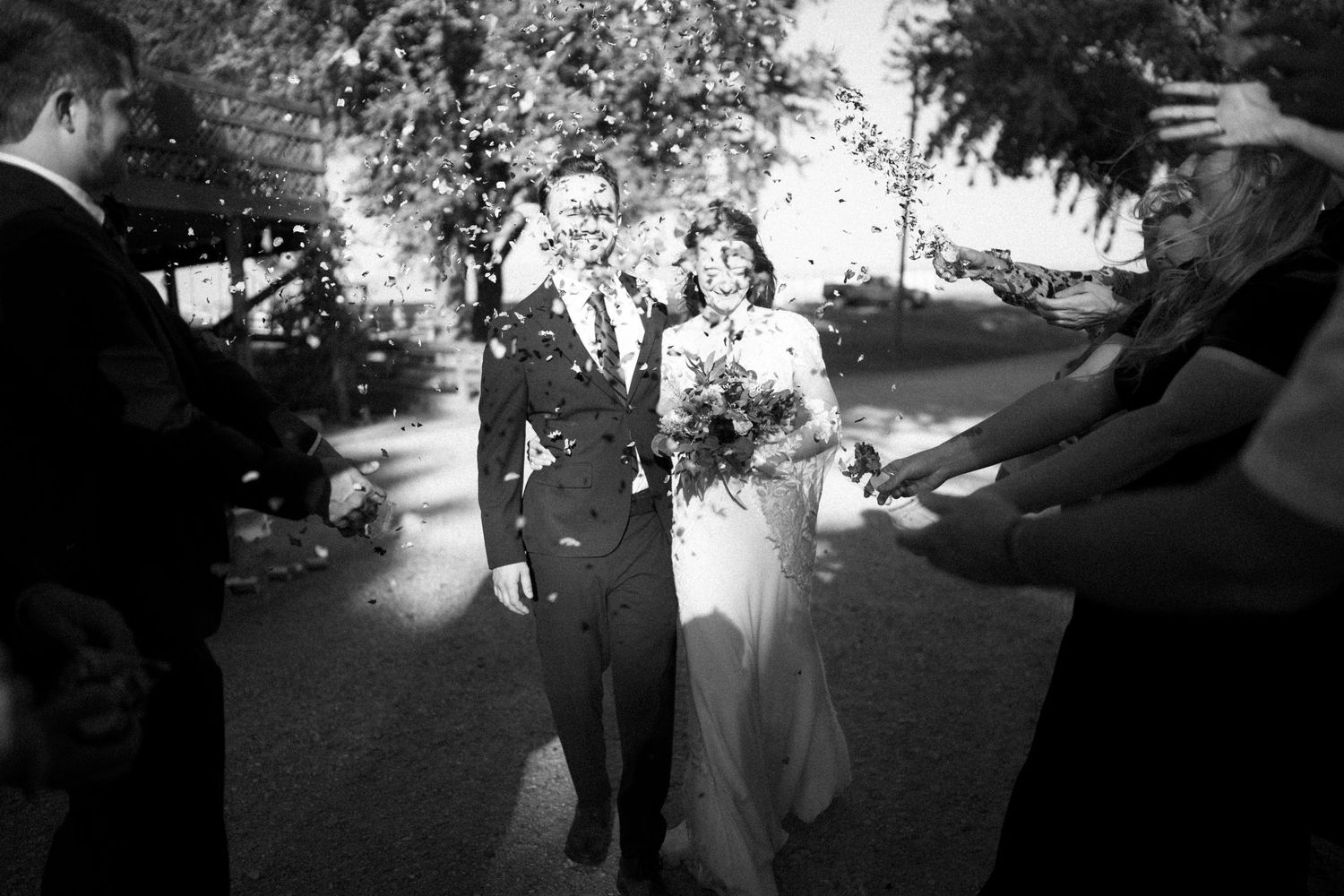 Black and white vintage photograph capturing newly married couple being celebrated at an outdoor wedding ceremony.