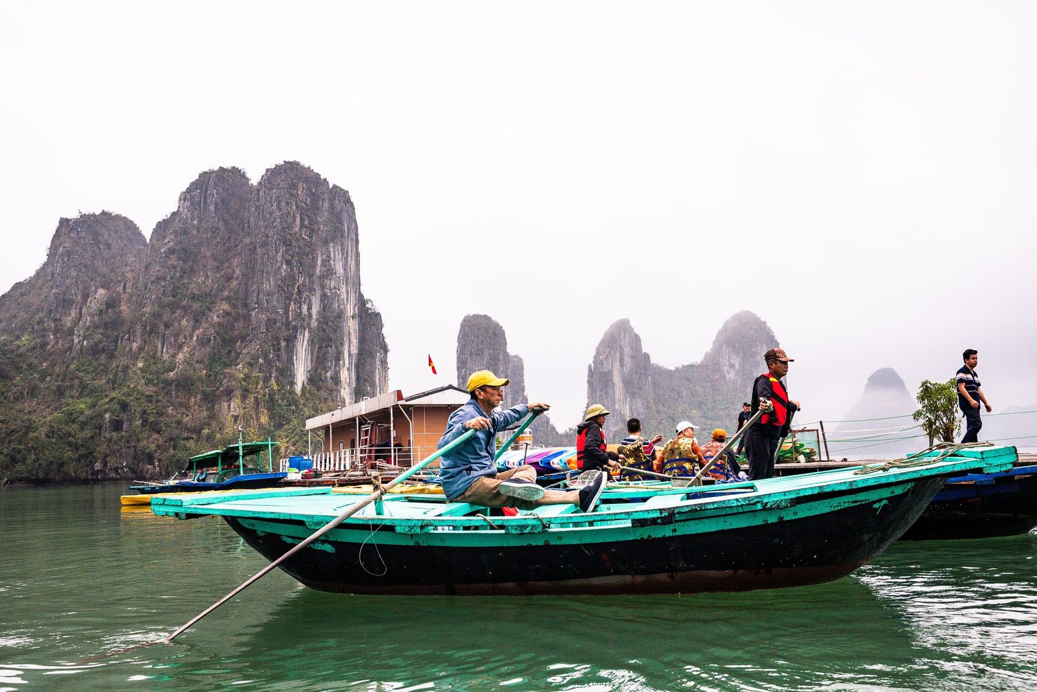 Tourists ride in traditional wooden boats through the limestone karsts of Ha Long Bay, Vietnam in misty weather.