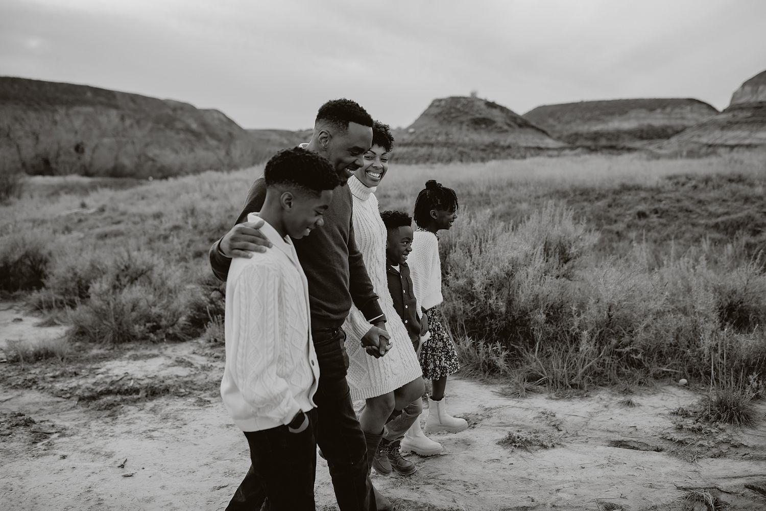 A couple embracing in a dramatic black and white landscape with rolling hills.