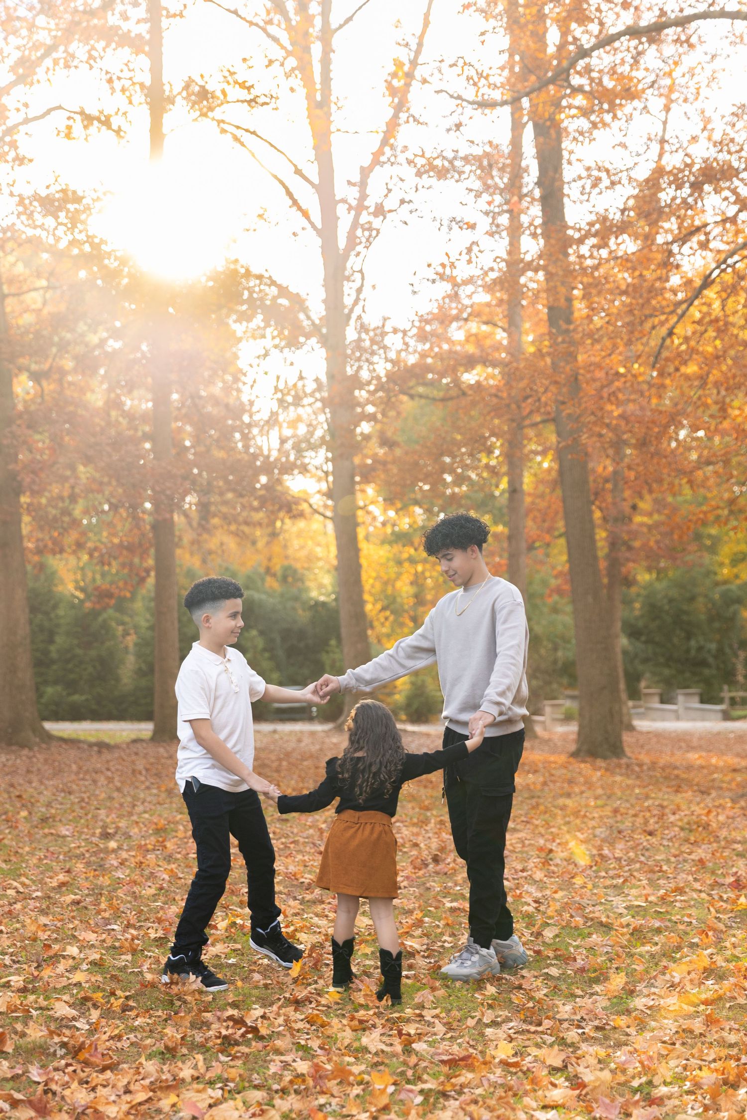Family playing together in autumn setting with fallen leaves and golden sunlight filtering through trees.
