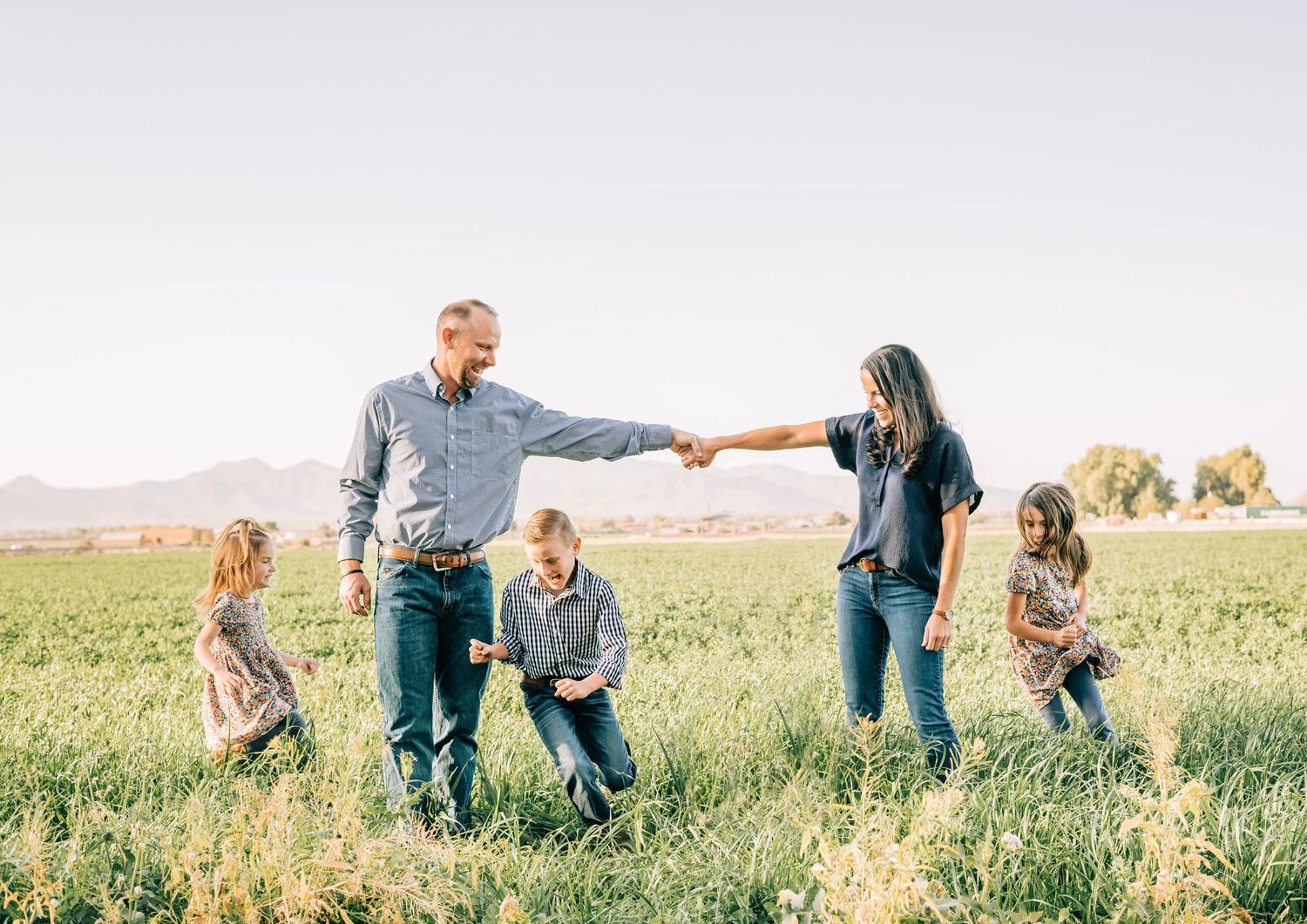 Family of five posing together in a lush green field with mountains in the background on a sunny day.