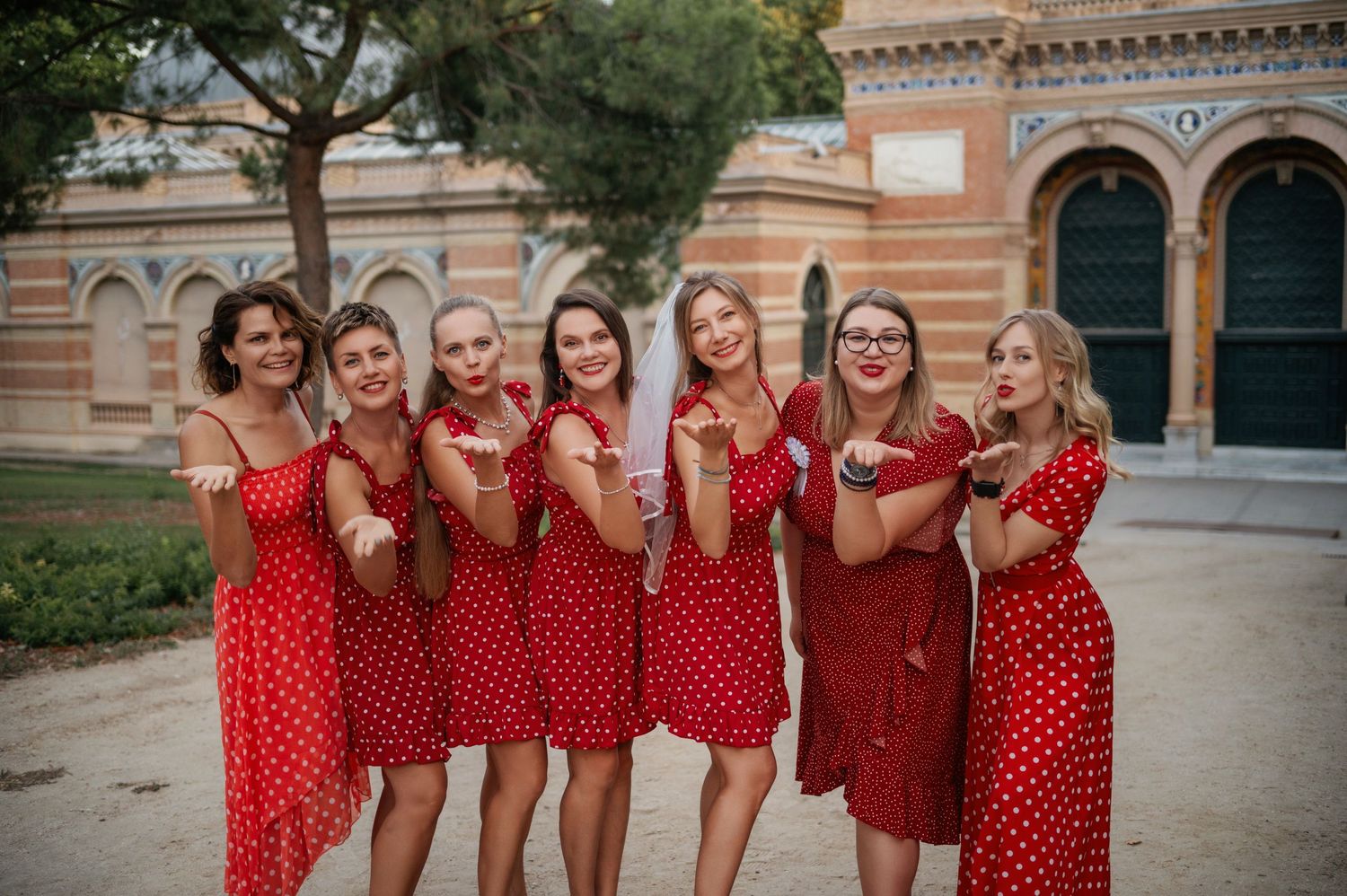 A group of bridesmaids wearing matching red and white polka dot dresses pose cheerfully outside a historic building.