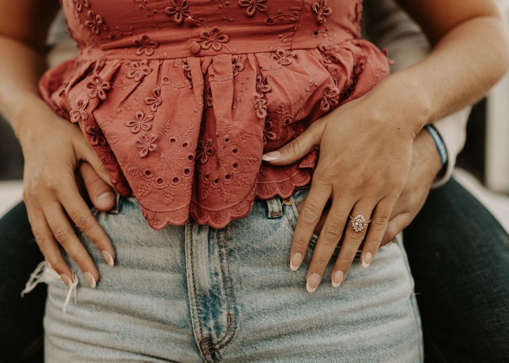 Close-up of hands resting on denim jeans waist wearing coral eyelet lace top.