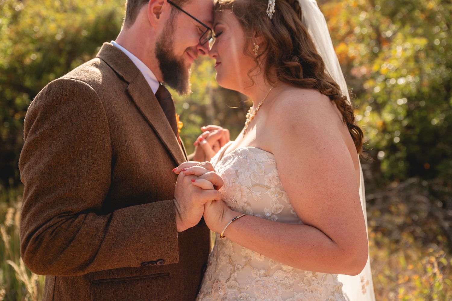 Couple sharing an intimate moment in warm sunlight wearing rustic wedding attire.