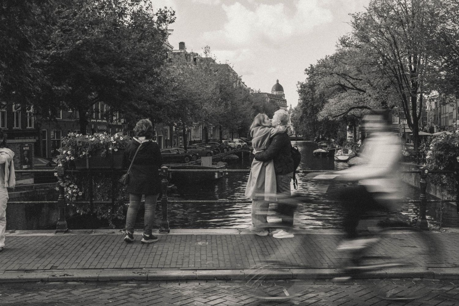 Black and white cinematic candid photo in Amsterdam – a couple kisses on a bridge.