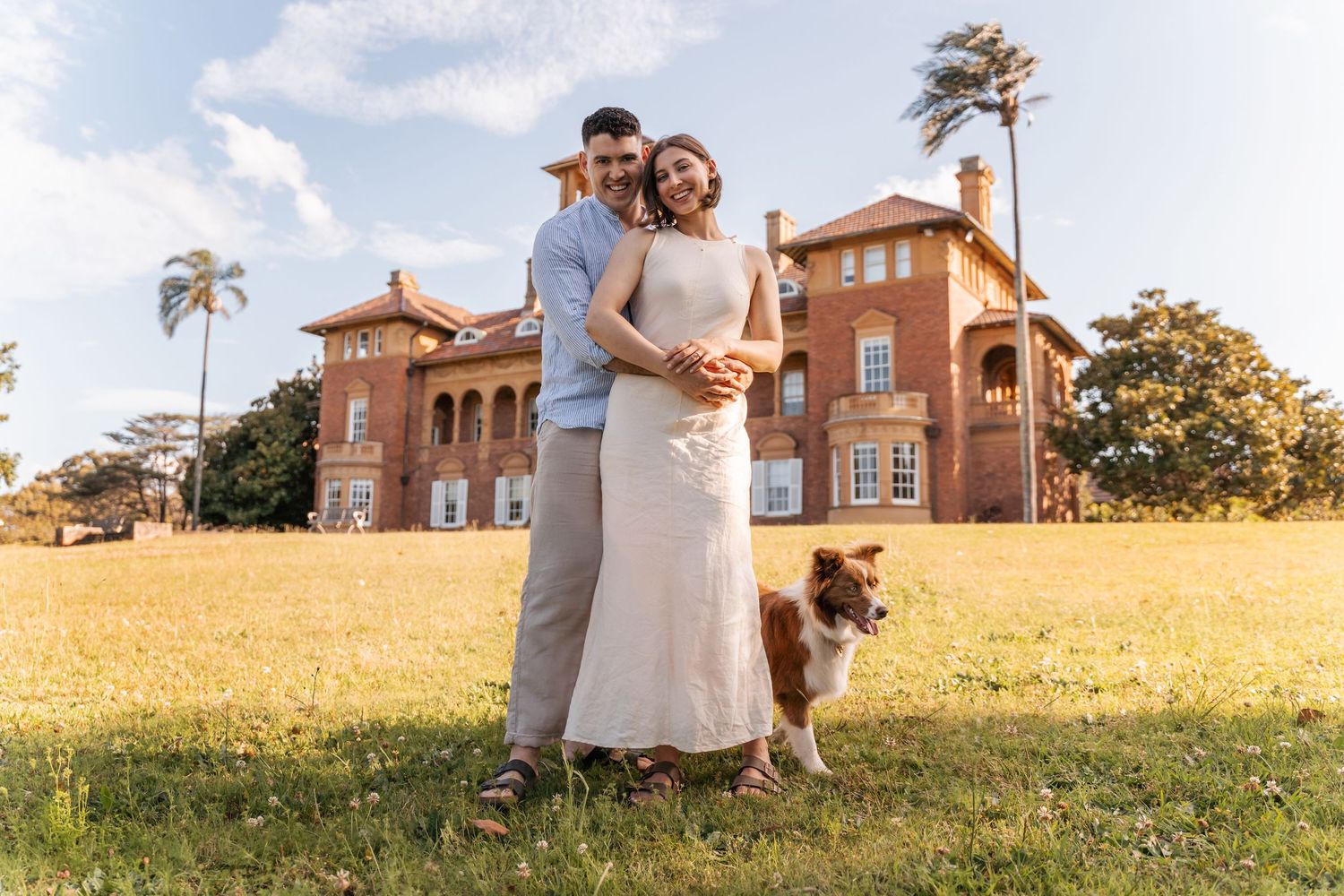 A couple stands in front of a rustic brick building during golden hour.
