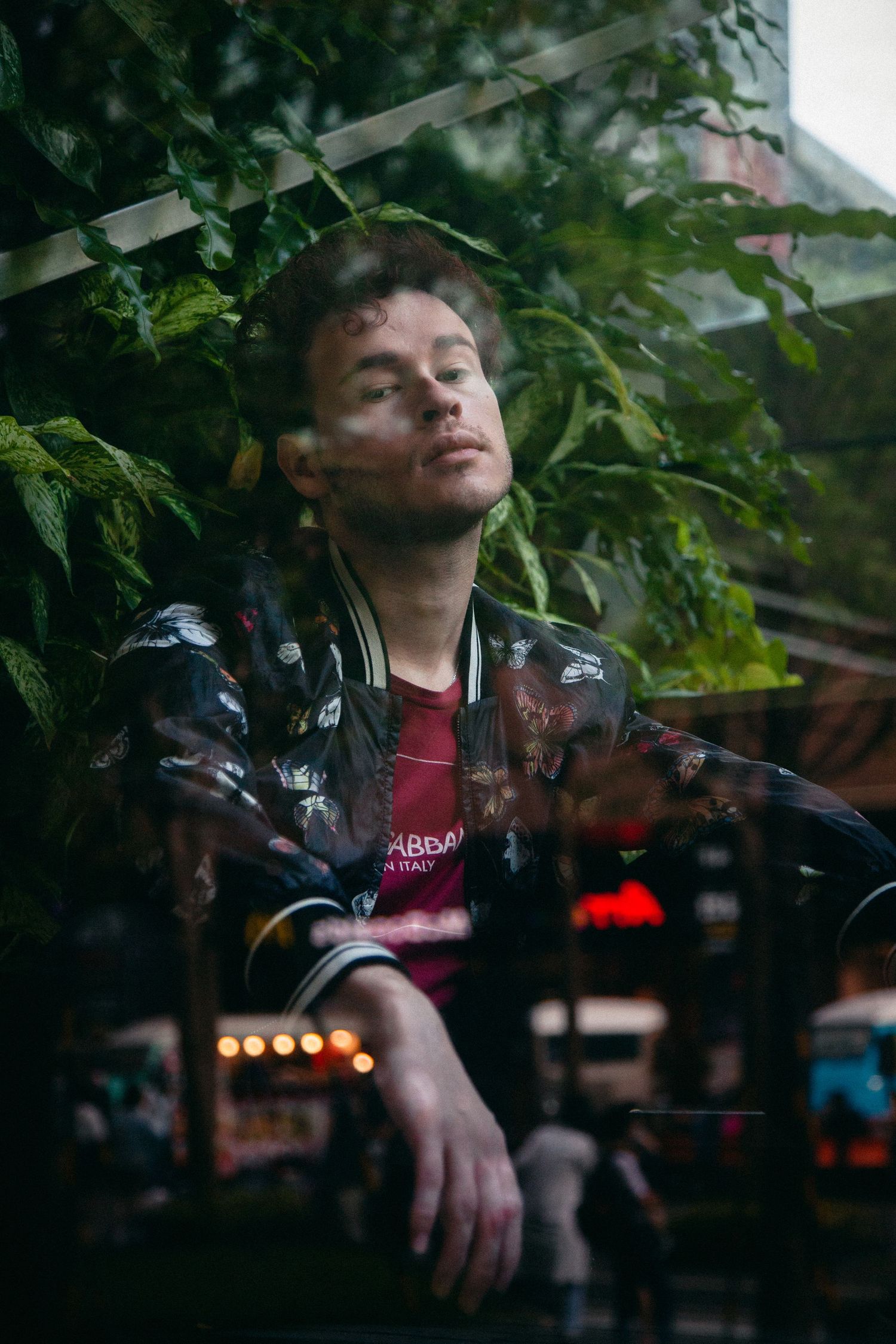 Young man in Dolce Gabbana jacket sitting pensively behind a glass window.