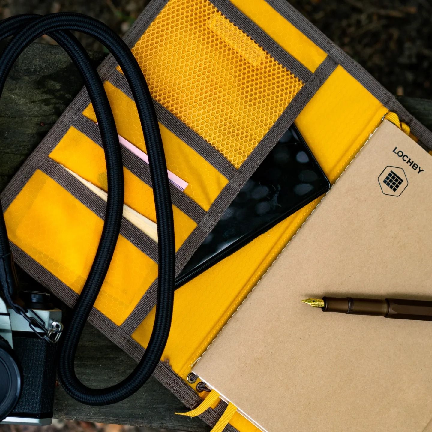 Yellow reflective gear, black camera strap, and notebook arranged on dark surface.
