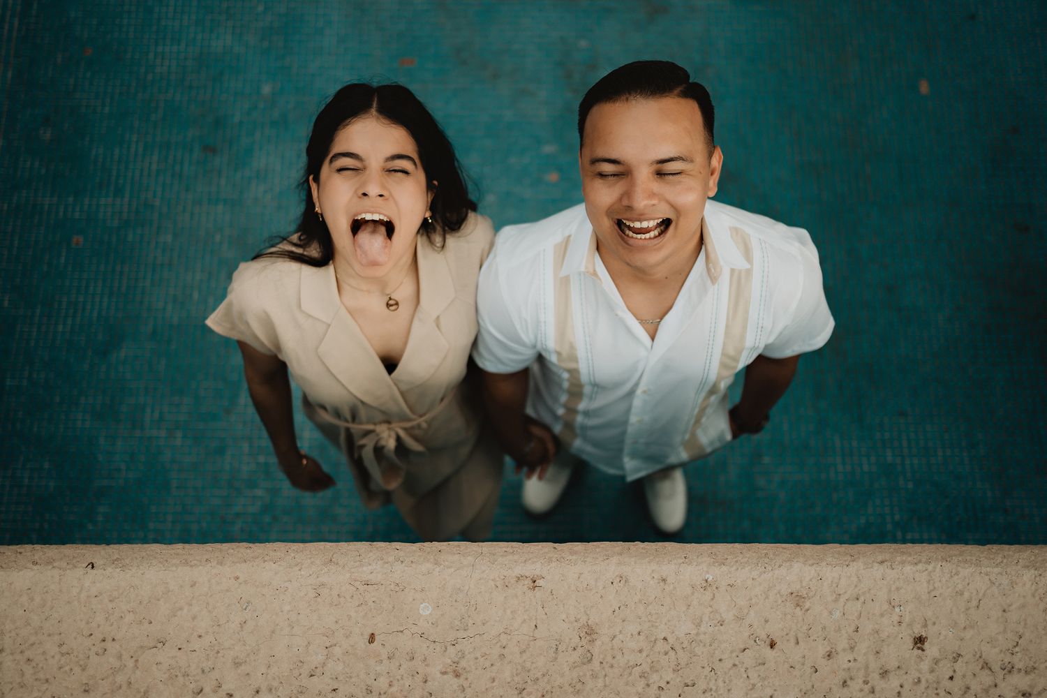 Couple looking up, making funny faces inside an empty pool, capturing a playful pre-wedding moment in Mazatlán