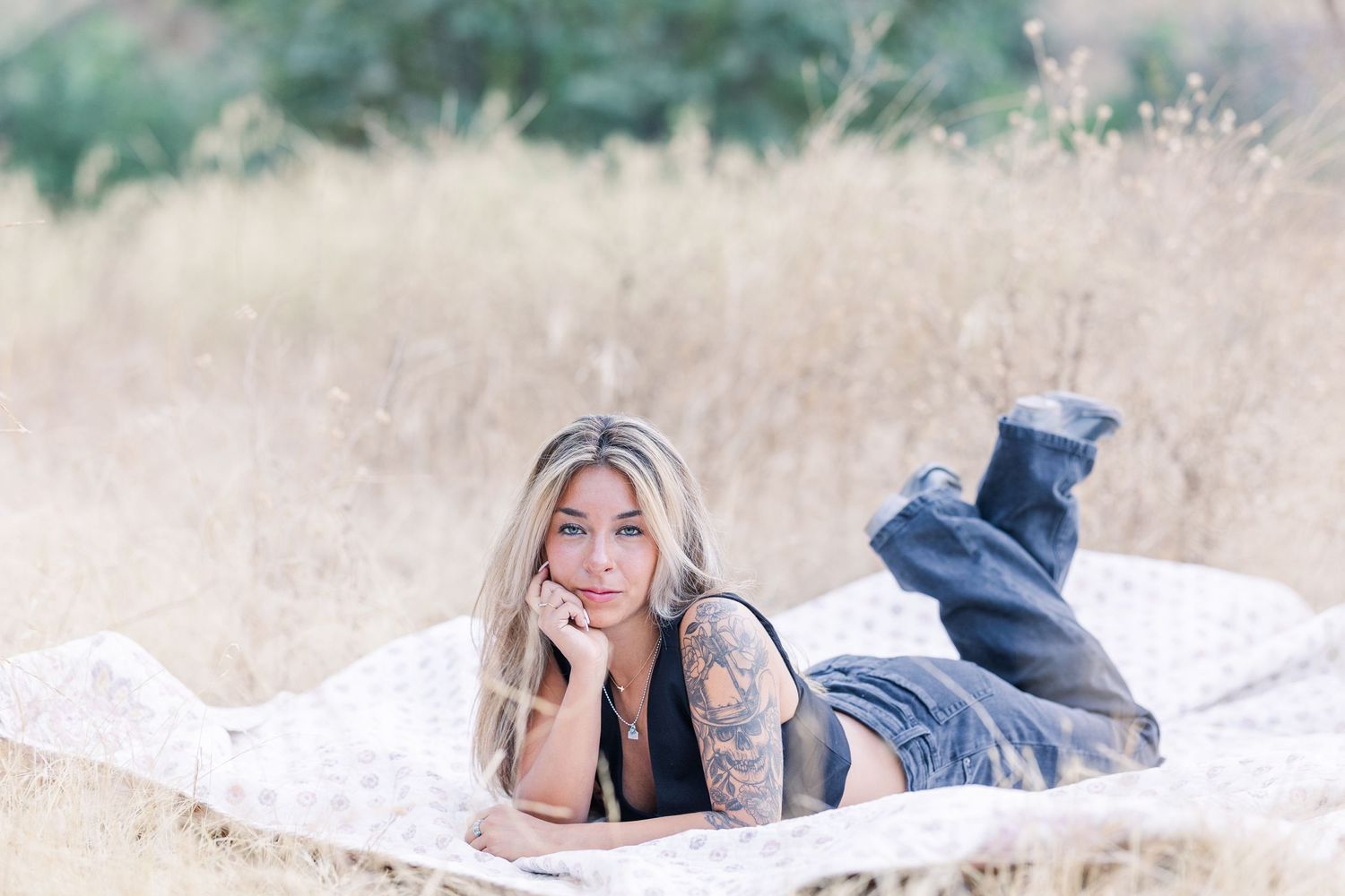 Casual portrait of someone laying on blanket in field wearing jeans and black top.
