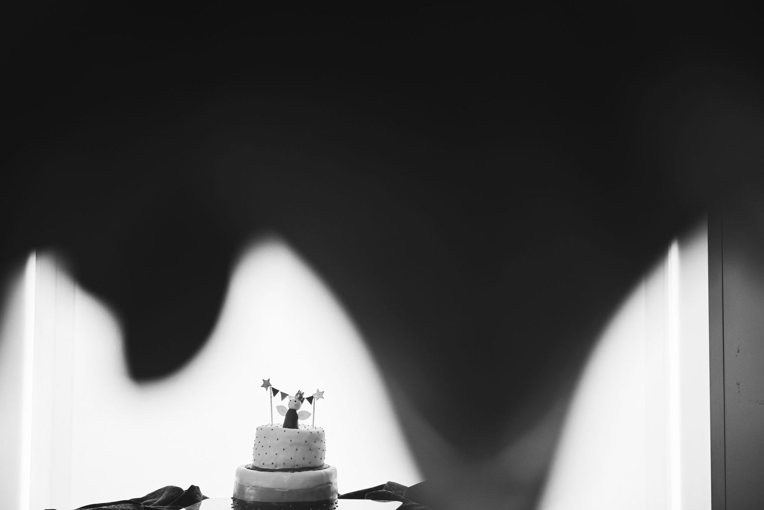 Black and white photo of a elegant tiered wedding cake displayed against a dramatic shadowed white wall backdrop.