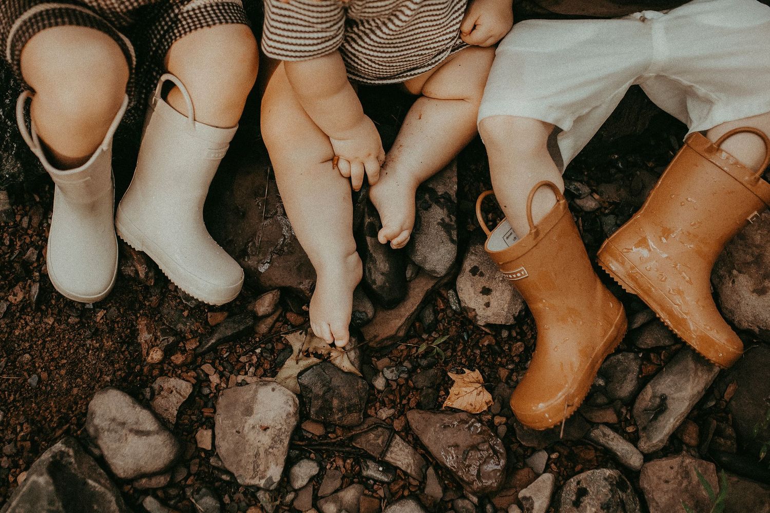 Row of feet and shoes lined up on dark soil ground.
