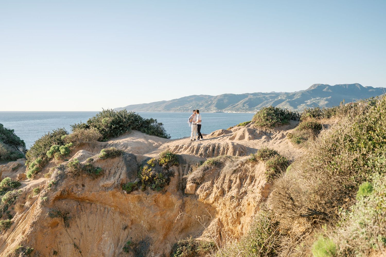 Scenic coastal cliffs overlooking the Pacific Ocean on a sunny day with rugged terrain and coastal vegetation.