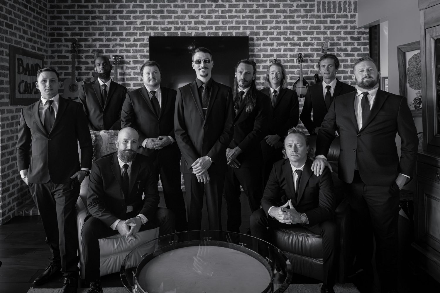 A vintage black and white photograph shows several people in formal attire gathered in front of a brick wall.