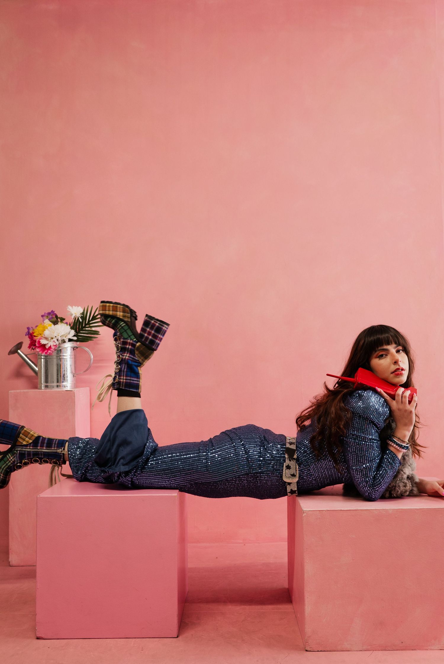 Someone in denim lying across pink geometric blocks against a pink wall in a creative fashion photo series.