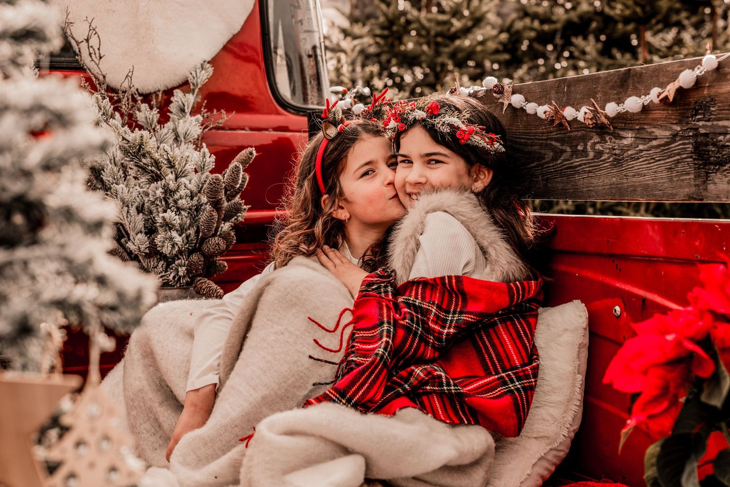 Cozy holiday scene with two figures embracing in front of a red vintage truck with winter decorations and flannel.