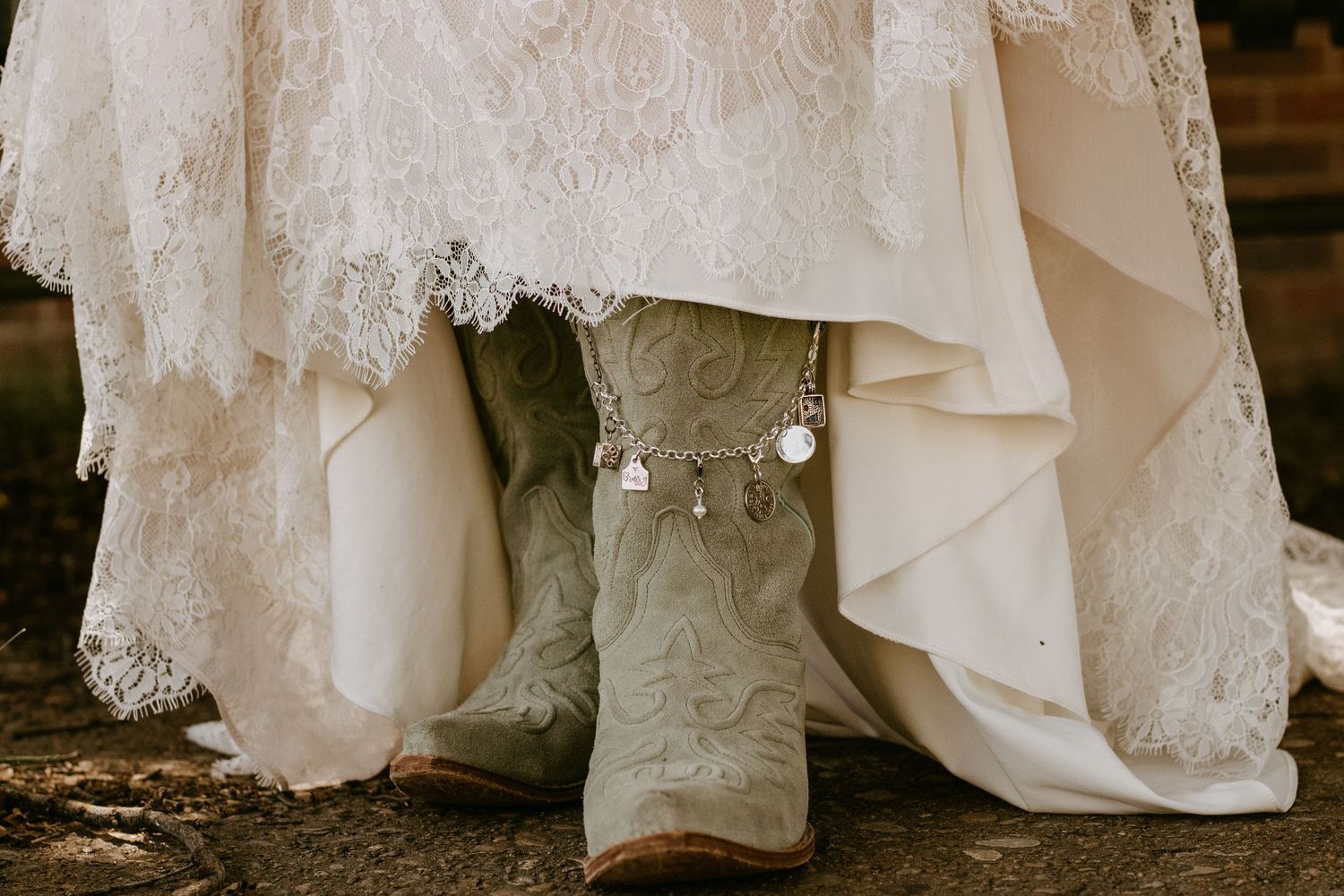 Bride wearing intricate lace wedding gown with embroidered cowboy boots and delicate anklet at rustic outdoor wedding.